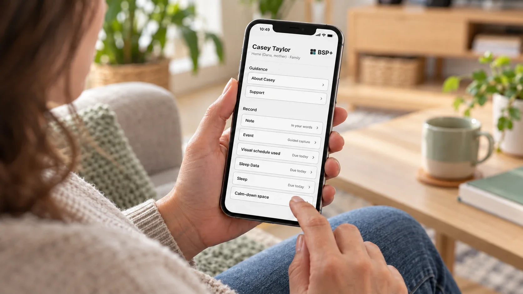 A support worker holds a phone showing BSP+ for Casey Taylor: guidance about Casey and Support, and Note, Event and monitoring items to record.